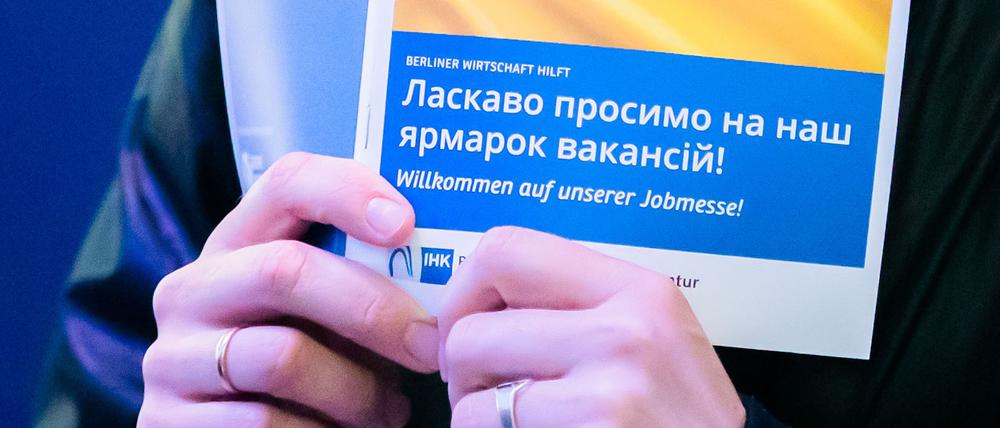 Eine Frau hält bei einer Jobmesse für ukrainische Geflüchtete von der IHK Berlin und der Agentur für Arbeit den Messeplan mit der ukrainischen Flagge.