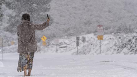Eine Frau steht auf einer schneebedeckten Straße und macht ein Selfie im Angeles National Forest in der Nähe von La Canada Flintridge. 