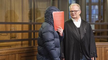 Ein 24 Jahre alter Mann hält sich im Gerichtssaal eine Mappe vor das Gesicht. Der Mann soll am 19. Mai 2022 nach dem Fußball-Relegationsspiel zwischen Hertha BSC und dem Hamburger SV in Berlin einem Hertha-Fan so heftig mit der Faust ins Gesicht geschlagen haben, dass dieser ungebremst zu Boden fiel und mit dem Hinterkopf auf dem Asphalt aufschlug. Der 55-Jährige erlitt ein schweres Schädel-Hirn-Trauma und starb wenige Tage später in einem Krankenhaus. 
