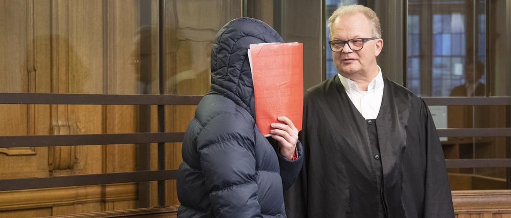 Ein 24 Jahre alter Mann hält sich im Gerichtssaal eine Mappe vor das Gesicht. Der Mann soll am 19. Mai 2022 nach dem Fußball-Relegationsspiel zwischen Hertha BSC und dem Hamburger SV in Berlin einem Hertha-Fan so heftig mit der Faust ins Gesicht geschlagen haben, dass dieser ungebremst zu Boden fiel und mit dem Hinterkopf auf dem Asphalt aufschlug. Der 55-Jährige erlitt ein schweres Schädel-Hirn-Trauma und starb wenige Tage später in einem Krankenhaus.