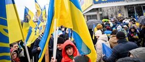 24.02.2023, Berlin: Teilnehmer einer Demonstration unter dem Motto «Wir werden nie vergessen» stehen an der Karl-Marx-Allee vor dem Cafe Moskau, das für ein paar Tage in Cafe Kyiv (Kiew) umbenannt wurde. 