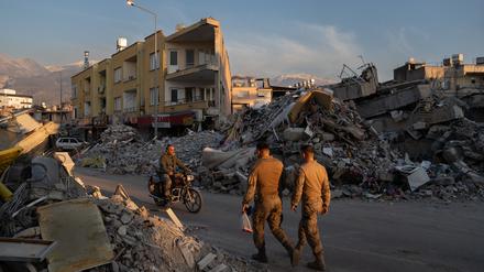 Menschen gehen an den Trümmern zerstörter Gebäude im türkisch-syrischen Grenzgebiet vorbei. 