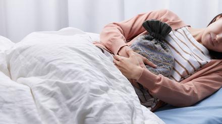 Wärmflasche und Bett. Viele menstruierende Personen sind an Tagen der Periode nicht arbeitsfähig.