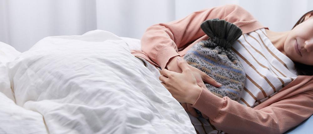 Wärmflasche und Bett. Viele menstruierende Personen sind an Tagen der Periode nicht arbeitsfähig.