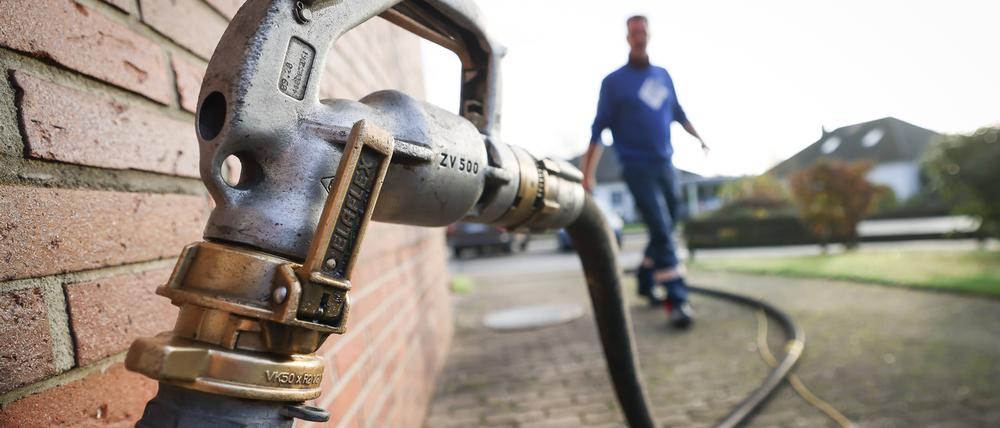 Ein Mitarbeiter eines Diesel- und Heizöl-Unternehmens geht zur Zapfpistole an einem Füllstutzen für die Heizöllieferung an einen Kunden in einem Einfamilienhaus. 