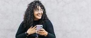 Junge Frau glücklich mit ihrem Handy vor einer Wand. 