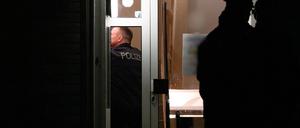 Polizisten stehen im Hausflur eines Mehrfamilienhauses und vor der Eingangstür. Bei einem Polizeieinsatz im brandenburgischen Senftenberg war hier in der vorletzten Woche ein Mann durch Schüsse von Beamten tödlich verletzt worden. Er soll sie mit einem „axtähnlichen Gegenstand“ angegriffen haben. Die Ermittlungen laufen.  