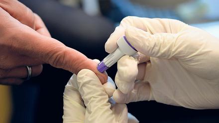 Mit einer Lanzette sticht der Apotheker in den Finger und nimmt anschließend Blut über die offene Wunde ab.