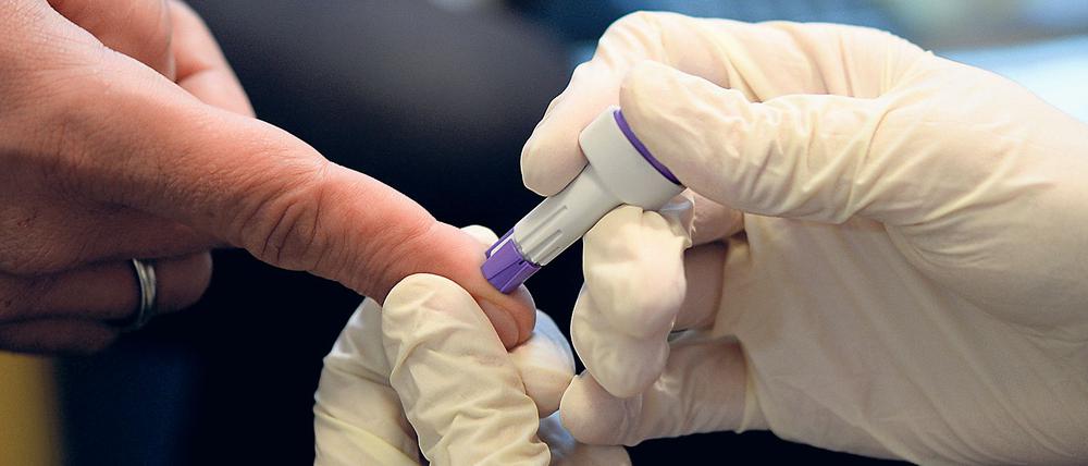 Mit einer Lanzette sticht der Apotheker in den Finger und nimmt anschließend Blut über die offene Wunde ab.