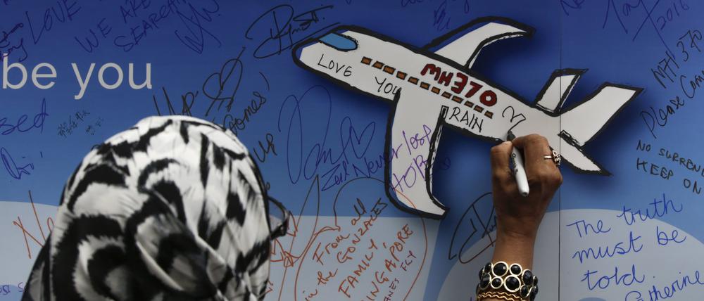 Eine Frau schreibt während einer Gedenkveranstaltung zum Flug MH370 eine Nachricht auf ein Banner.
