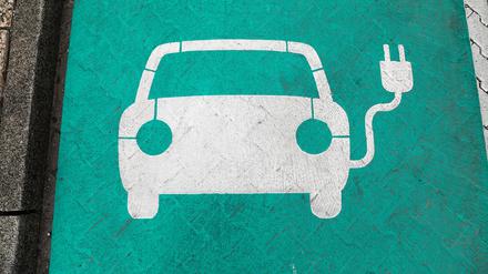 Ein stilisiertes Auto auf grünem Grund markiert einen Parkplatz mit Ladesäule für Elektrofahrzeuge.