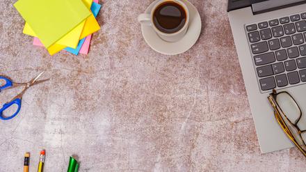 Bürotisch mit Laptop und anderen Arbeitsgeräten mit Kaffeetasse.