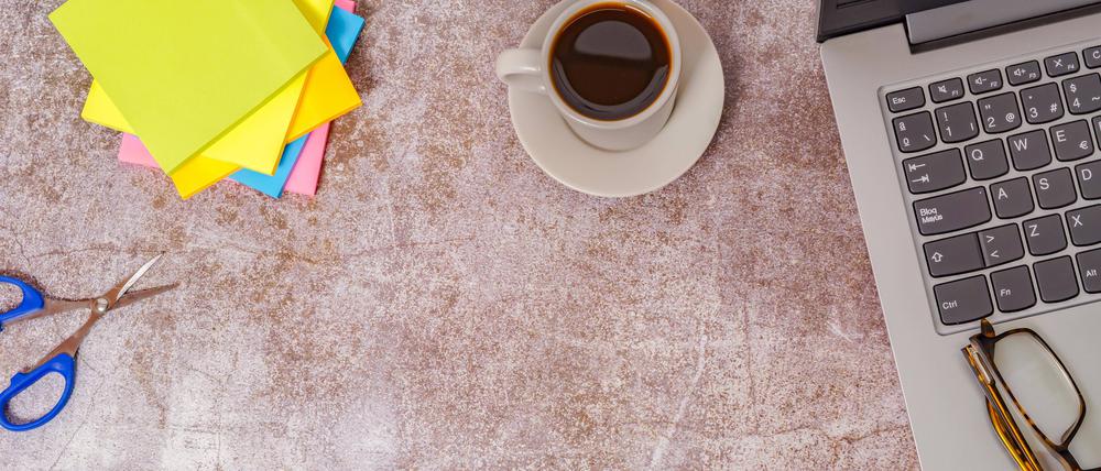 Bürotisch mit Laptop und anderen Arbeitsgeräten mit Kaffeetasse.