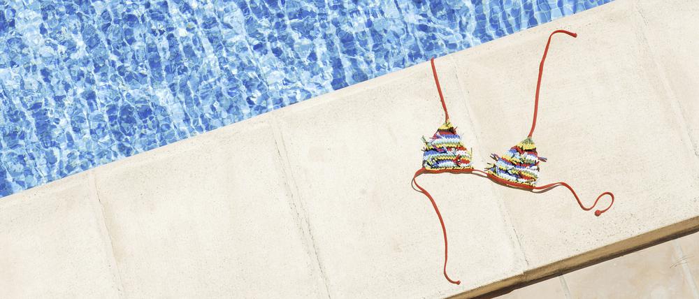 Ein Bikini-Oberteil liegt am Rand eines Schwimmbeckens.