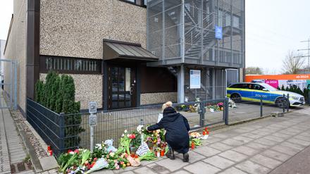 Eine Frau kniet an den Blumen und Kerzen vor dem Eingangsbereich einer Kirche der Zeugen Jehovas.