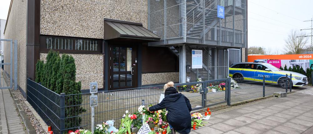 Eine Frau kniet an den Blumen und Kerzen vor dem Eingangsbereich einer Kirche der Zeugen Jehovas.