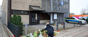 Eine Frau kniet an den Blumen und Kerzen vor dem Eingangsbereich einer Kirche der Zeugen Jehovas.