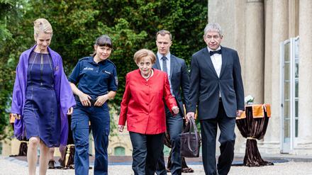 Katharina von Baugenwitz (Judith Engel, l.), die Polizistin Lena Amado (Svenja Liesau, 2. v. l.), Miss Merkel (Katharina Thalbach, 3. v. l.), ihr Personenschützer Mike (Tim Kalkhof, 2. v. r.), sowie Merkels Ehemann Joachim Sauer (Thorsten Merten, r.) befinden sich auf dem Weg zum Fest im Schlosshof, wo derzeit ein reges Treiben herrscht. Die Verwendung des sendungsbezogenen Materials ist nur mit dem Hinweis und Verlinkung auf RTL+ gestattet.