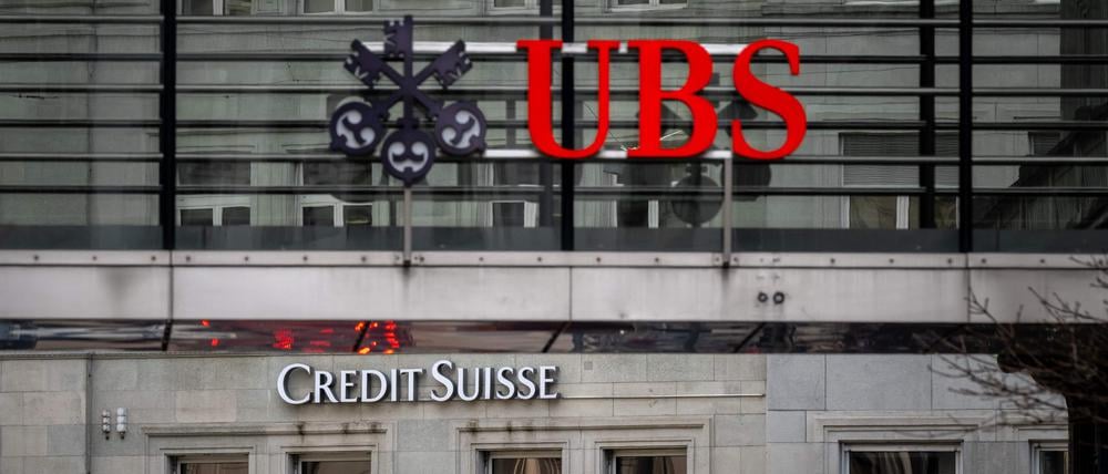 Nun Verknüpft – das Logo der „UBS“ auf einem Gitter vor einer Hauswand mit dem Schriftzug von „Credit Suisse“.