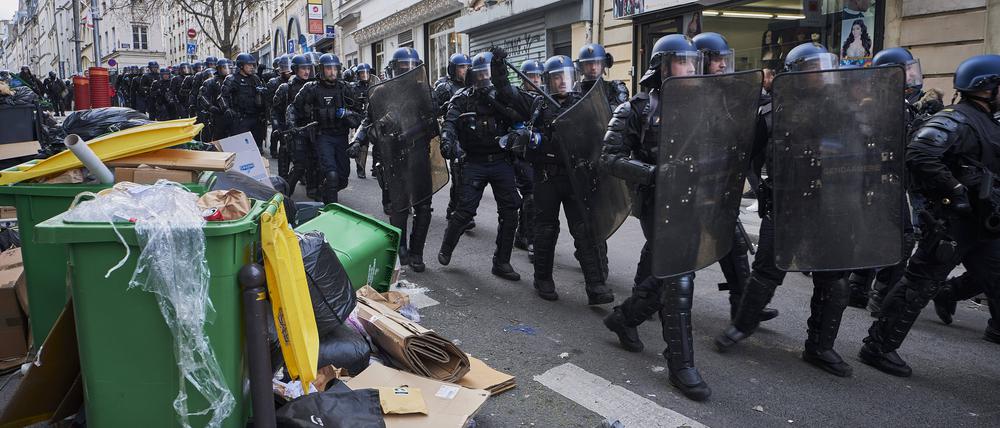 Polizisten marschieren durch die Straßen von Paris, in denen sich der liegen gebliebene Müll türmt.