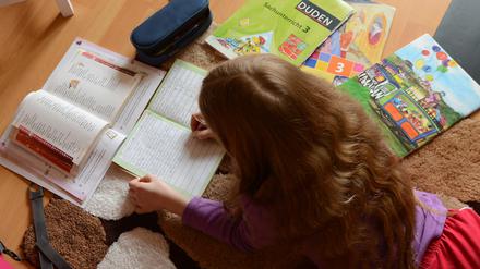 Ein achtjähriges Mädchen liegt auf einem Teppich in ihrem Kinderzimmer und erledigt Hausaufgaben im Fach Deutsch.