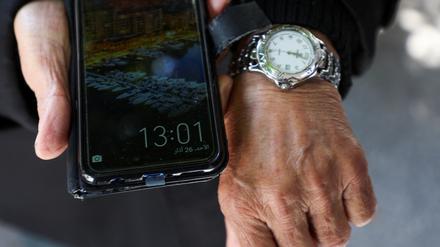 Ein Mann zeigt die unterschiedlichen Uhrzeiten auf seinem Handy und seiner Armbanduhr. 