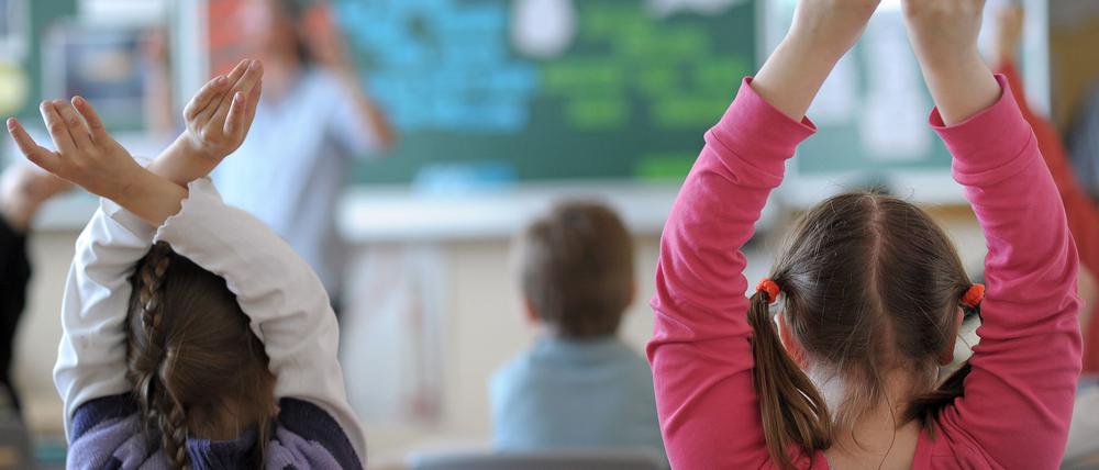 Zwei Schülerinnen melden sich während des Unterrichts in einem Klassenzimmer der Grundschule.