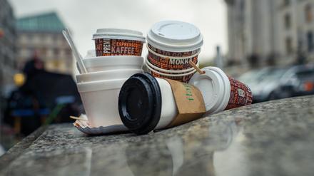 Einweg-Kaffeebecher und Plastikschalen stapeln sich an einem Gehweg. 
