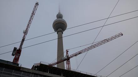  Die Spitze des Berliner Fernsehturms am Alexanderplatz im Bezirk Mitte verschwindet im Nebel, während im Vordergrund eine Baustelle und Baukräne zu sehen sind. 