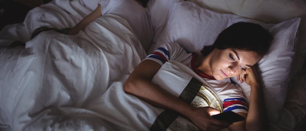 Woman using mobile phone while lying on bed at bedroom