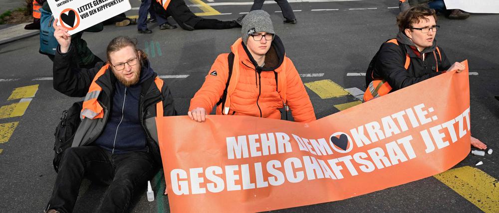 Activists of the environmental group "Last Generation" (Letzte Generation) are glued on the ground with a banner reading "More democracy: Society Council now", while police remove fellow activists (background) during a protest for climate change on April 5, 2023  in Berlin’s Charlottenburg district. (Photo by Tobias SCHWARZ / AFP)