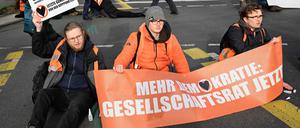 Activists of the environmental group "Last Generation" (Letzte Generation) are glued on the ground with a banner reading "More democracy: Society Council now", while police remove fellow activists (background) during a protest for climate change on April 5, 2023  in Berlin’s Charlottenburg district. (Photo by Tobias SCHWARZ / AFP)