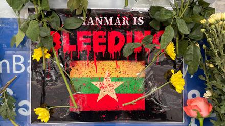 Vor der Flagge von Myanmar liegen Blumen. 