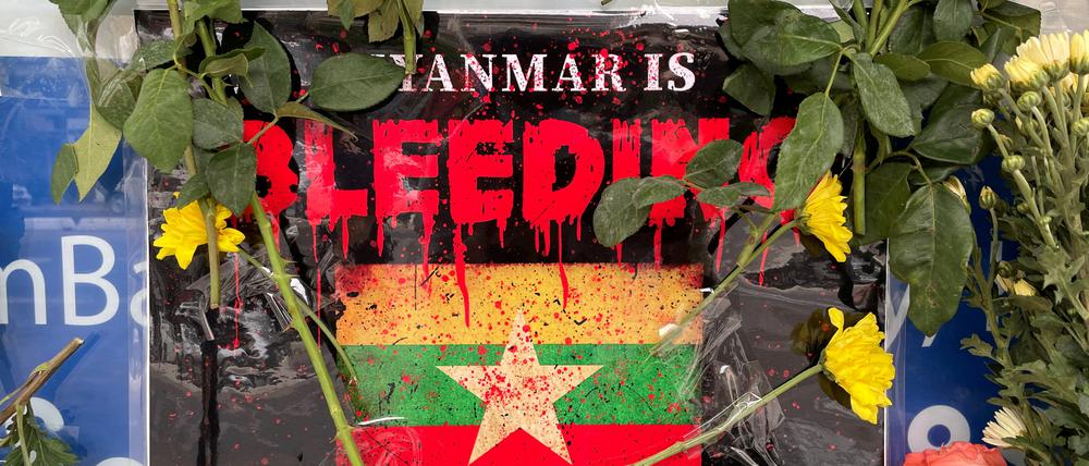 Vor der Flagge von Myanmar liegen Blumen. 