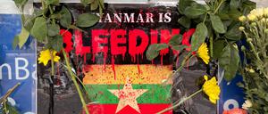 Vor der Flagge von Myanmar liegen Blumen. 