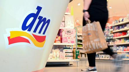 Eine Person geht in einer Filiale der Drogeriemarktkette dm mit einer Einkaufstüte am Kassenbereich vorbei.