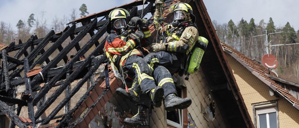 Zwei Feuerwehrleute werden mit Hilfe einer Drehleiter aus dem ausgebrannten Dachstuhl herausgehoben.