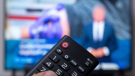 Ein Mann hält eine Fernbedienung vor einen Fernseher, auf dem die Tagesschau läuft. 