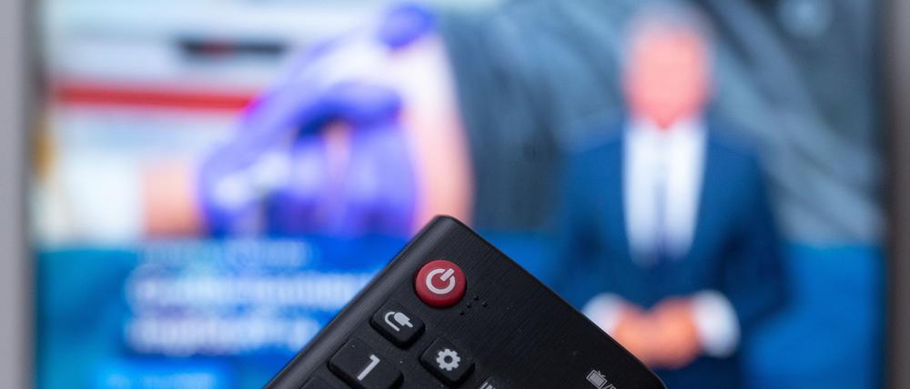 Ein Mann hält eine Fernbedienung vor einen Fernseher, auf dem die Tagesschau läuft.