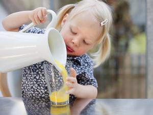 Ein kleines Kind mit blonden Zöpfen versucht, Saft in ein Glas einzuschenken.
