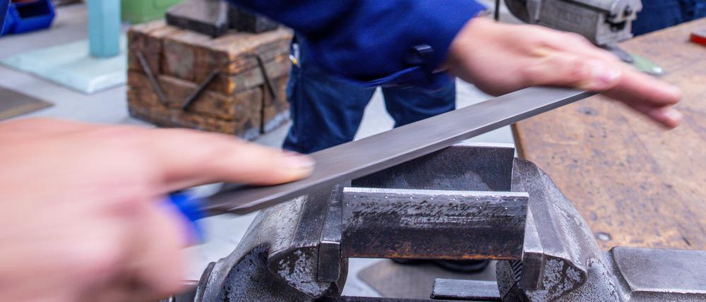 Lehrlinge arbeiten mit der Metallfeile an Schraubstöcken in einer Lehrwerkstatt. 