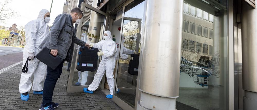 Ein Beamter in zivil bringt den vor Ort anwesenden Beamten der Spurensicherung technisches Equipment zum Tatort.
