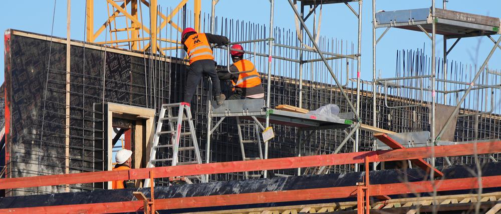 Drei Männer arbeiten auf einer Etage eines Rohbaus für Wohn- und Geschäftshäuser.