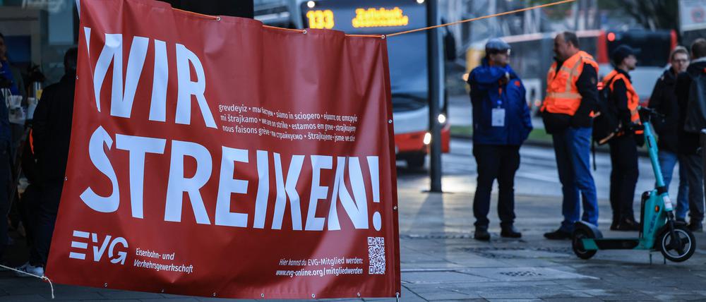 Mitglieder der Bahngewerkschaft EVG stehen in der Nähe des Bahnhofs Köln an einem Transparent mit der Aufschrift „Wir streiken“.