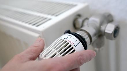Eine Frau dreht an einem Heizungsthermostat.  