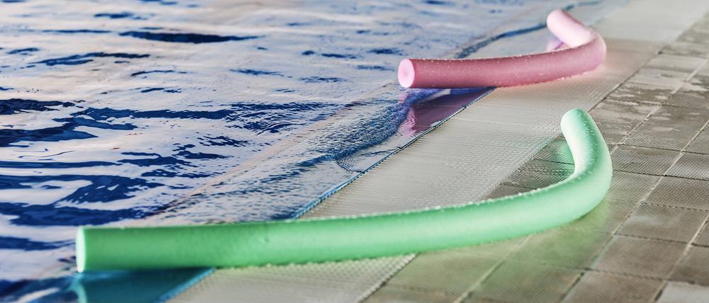Green and pink foam aqua noodles placed near swimming pool for water aerobics training