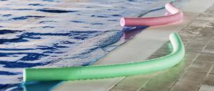 Green and pink foam aqua noodles placed near swimming pool for water aerobics training