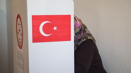 Eine Frau mit Kopftuch steht in einem Wahllokal in einer Wahlkabine.