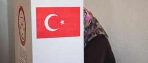 Eine Frau mit Kopftuch steht in einem Wahllokal in einer Wahlkabine.