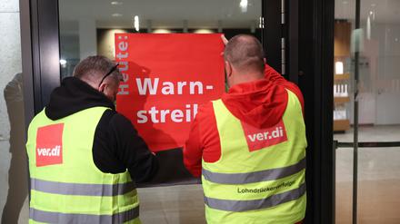 dpatopbilder - 24.04.2023, Berlin: Streikende befestigen ein Plakat mit der Aufschrift "Warnstreik" am Terminal des Flughafens BER. Seite heute Morgen 03:30 Uhr wird am Flughafen gestreikt. Alle abgehenden Flüge wurden gestrichen. Foto: Jörg Carstensen/dpa +++ dpa-Bildfunk +++